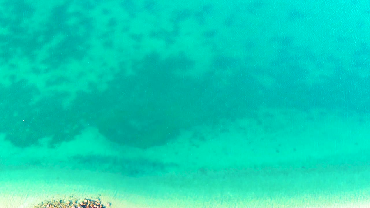 Turquoise water over sand and dark coral patches