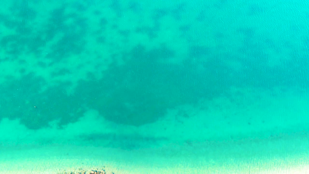 Turquoise water covers a pale sandy seabed in Bahia De Los Angeles, Mexico, with darker coral shapes spread across the upper half and no visible people.