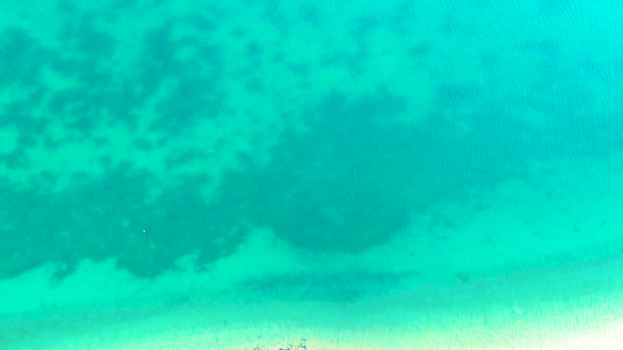 Overhead turquoise ocean in Bahia De Los Angeles, Mexico, shows darker coral areas on the left, pale sand along the lower edge, and no visible people.