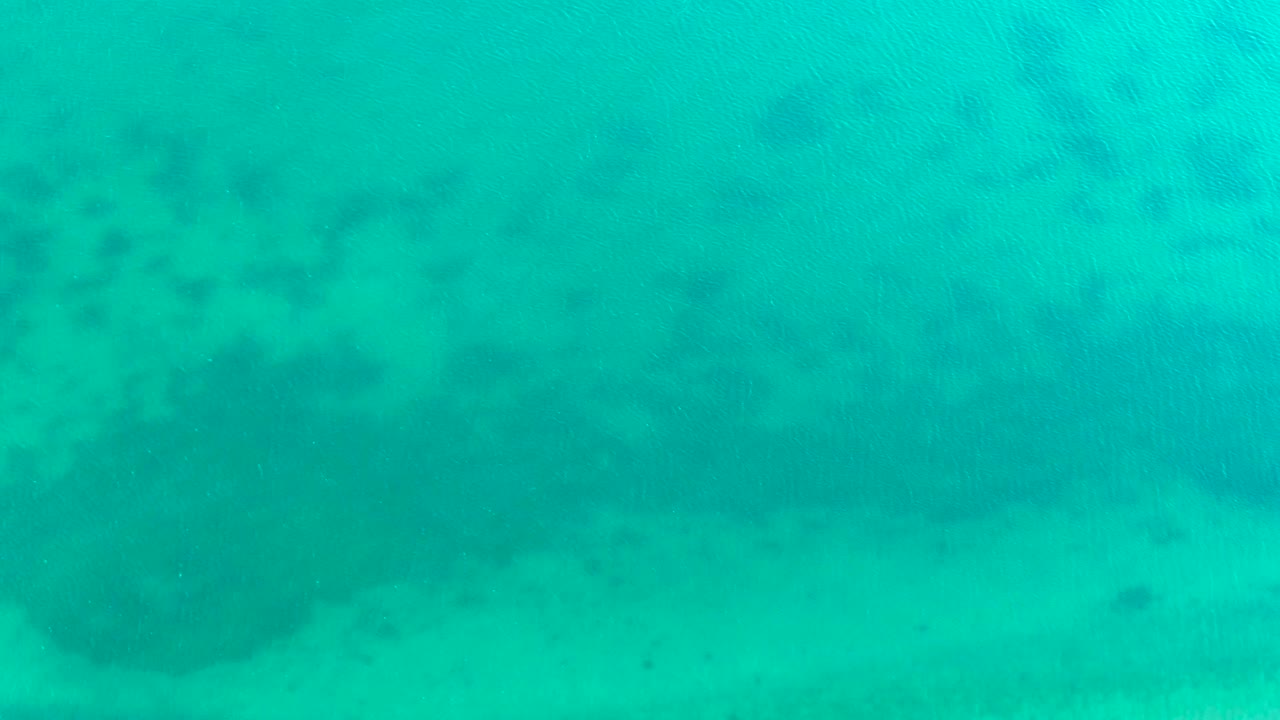 Turquoise water and sandy seabed with darker patches near the edge.