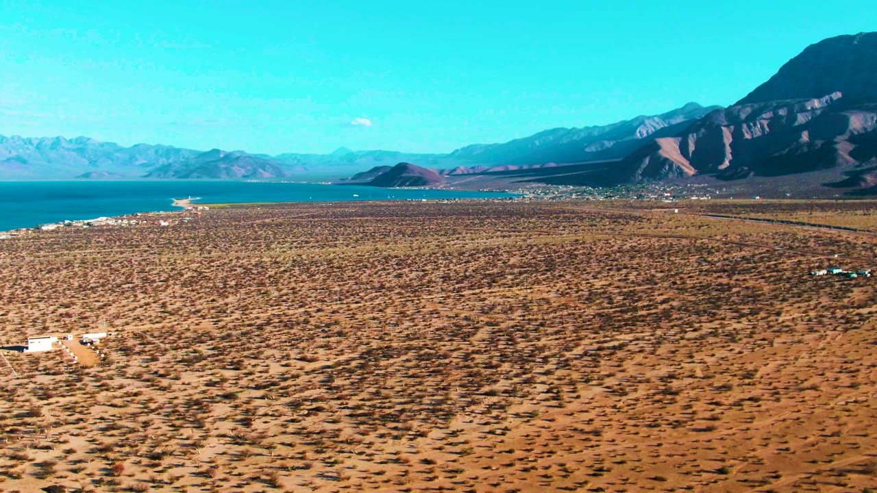 Wide aerial view of dry scrub plain, blue water, and distant mountains.