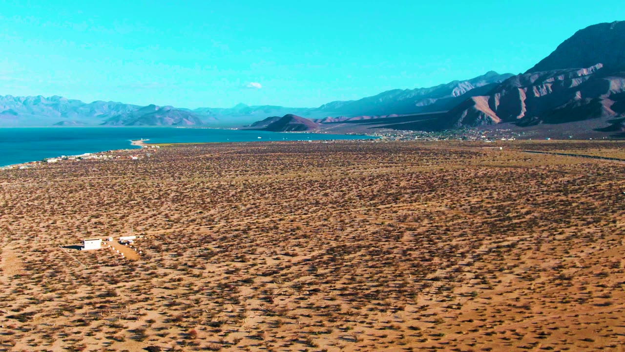 White vehicle on a dirt track across a dry plain near a blue bay.
