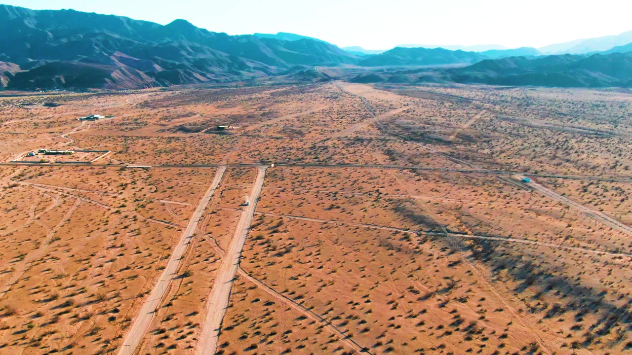 Aerial desert runway crossing scrubland toward distant mountains.