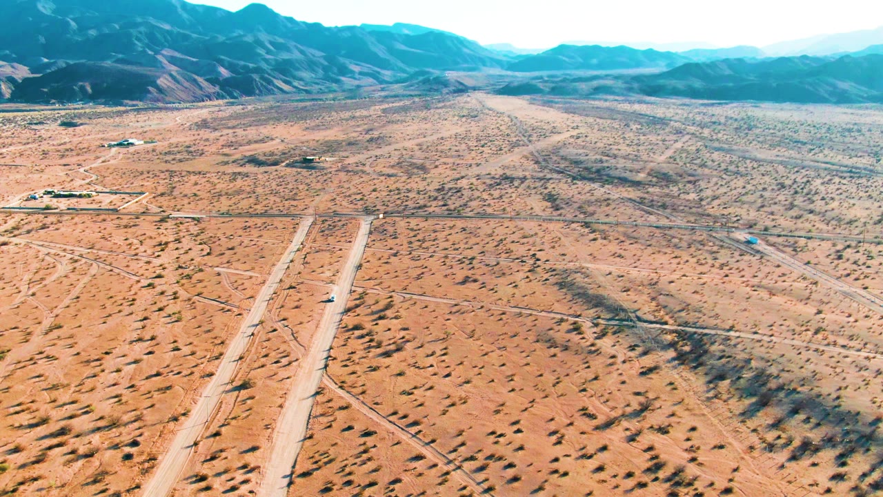 At 0:02, the aerial view in Bahia De Los Angeles keeps the runway in the lower frame as the car moves along it, backed by sparse desert vegetation, low buildings, mountains, and no visible people.