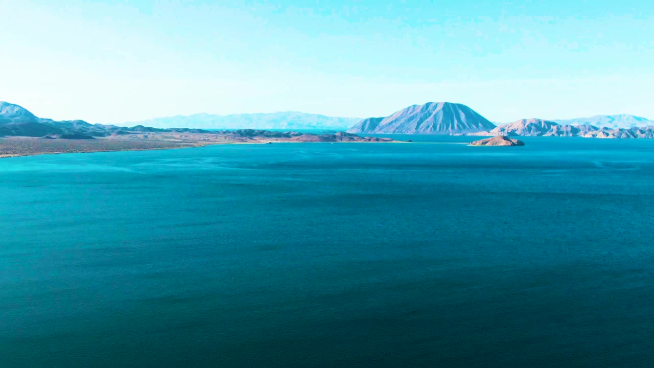 Wide aerial view of blue water with distant islands and mountains.