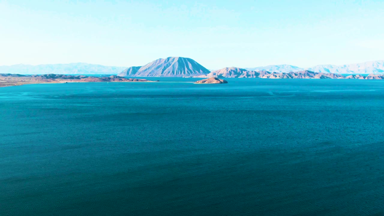 Open blue bay with island forms and mountains under clear sky.