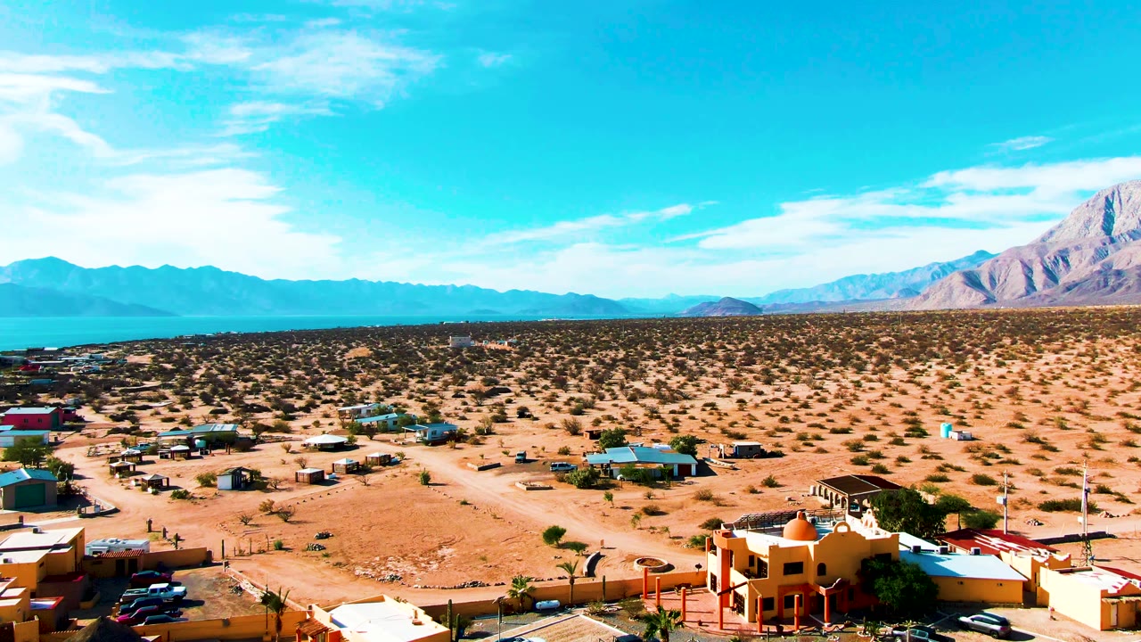 Elevated desert town view with houses, open lots, and blue horizon.