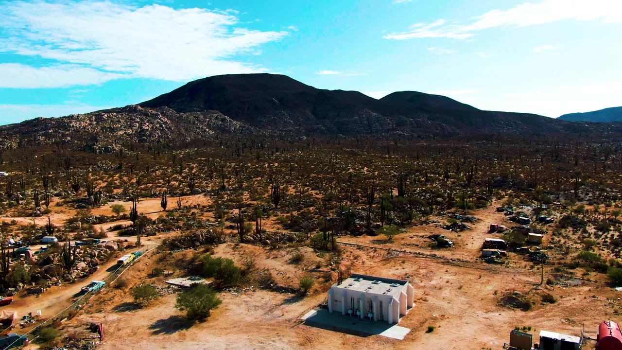 Higher aerial view of cactus desert, small building, dirt roads, and mountains