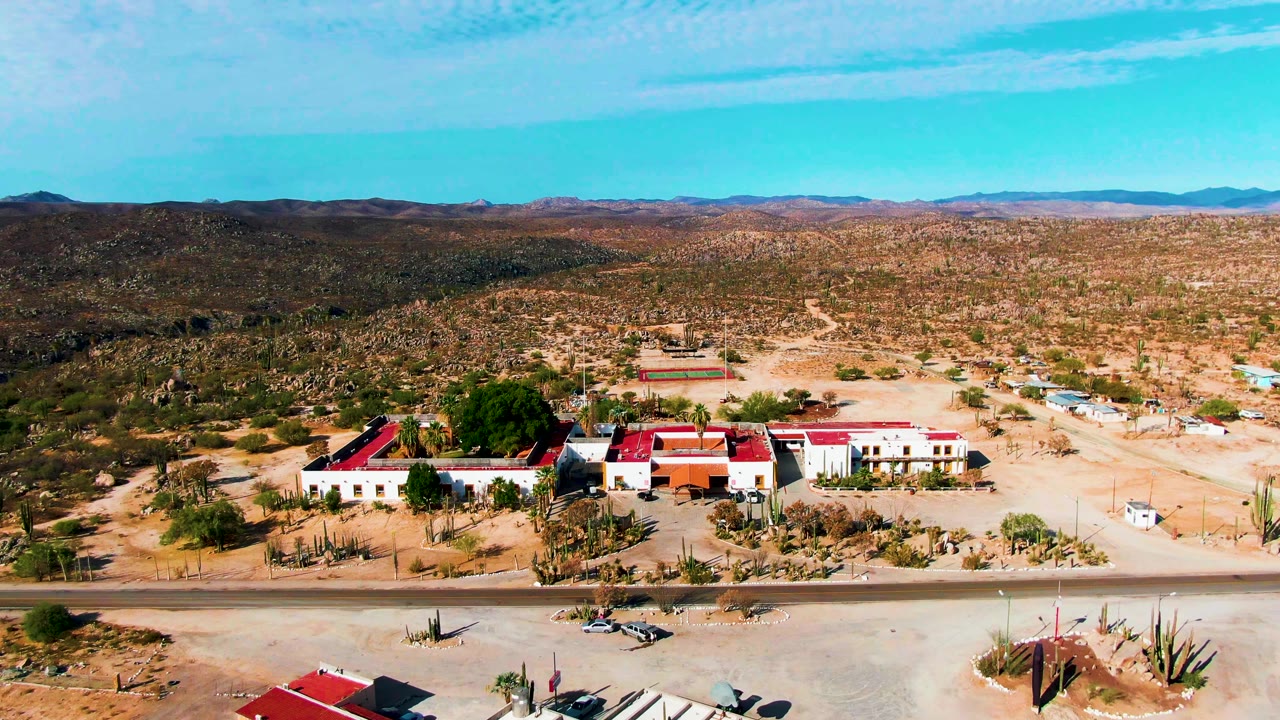 The second frame keeps the Catavina BC Mexico buildings low in the view, with cactus clusters, an empty road, broad desert scrub, mountain ridges, and no visible people.