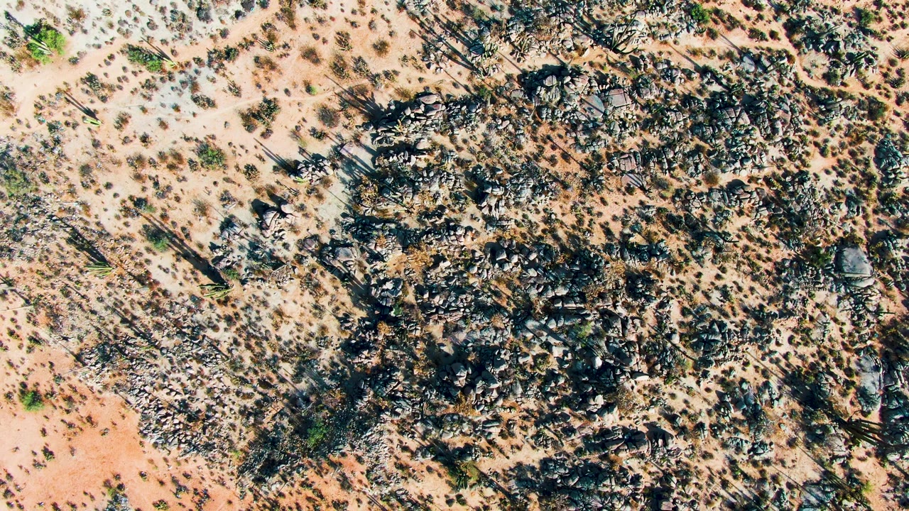 Overhead view of Catavina BC Mexico desert terrain with tan soil, dark rock clusters, scattered shrubs, and no visible people.