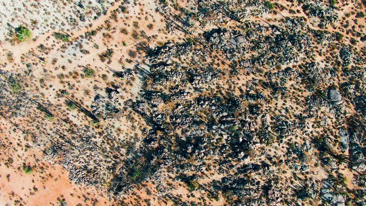 Straight-down view of Catavina BC Mexico desert with broken dark rocks, reddish-tan soil, scattered brush, and no visible people.