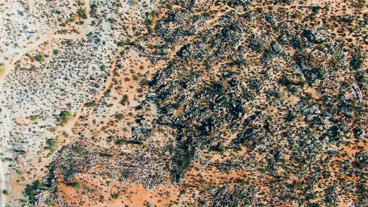 Overhead desert terrain with large dark rock field and shrubs.