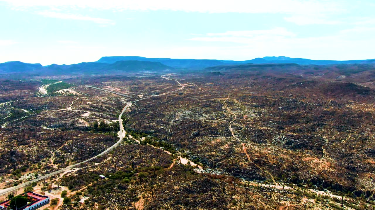 Aerial view over Catavina BC Mexico showing pale roads winding through brown and green desert hills toward distant mountains, with no visible people.
