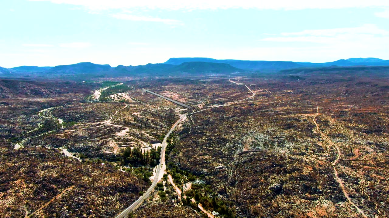 Aerial road corridor through brown and green mountain terrain.