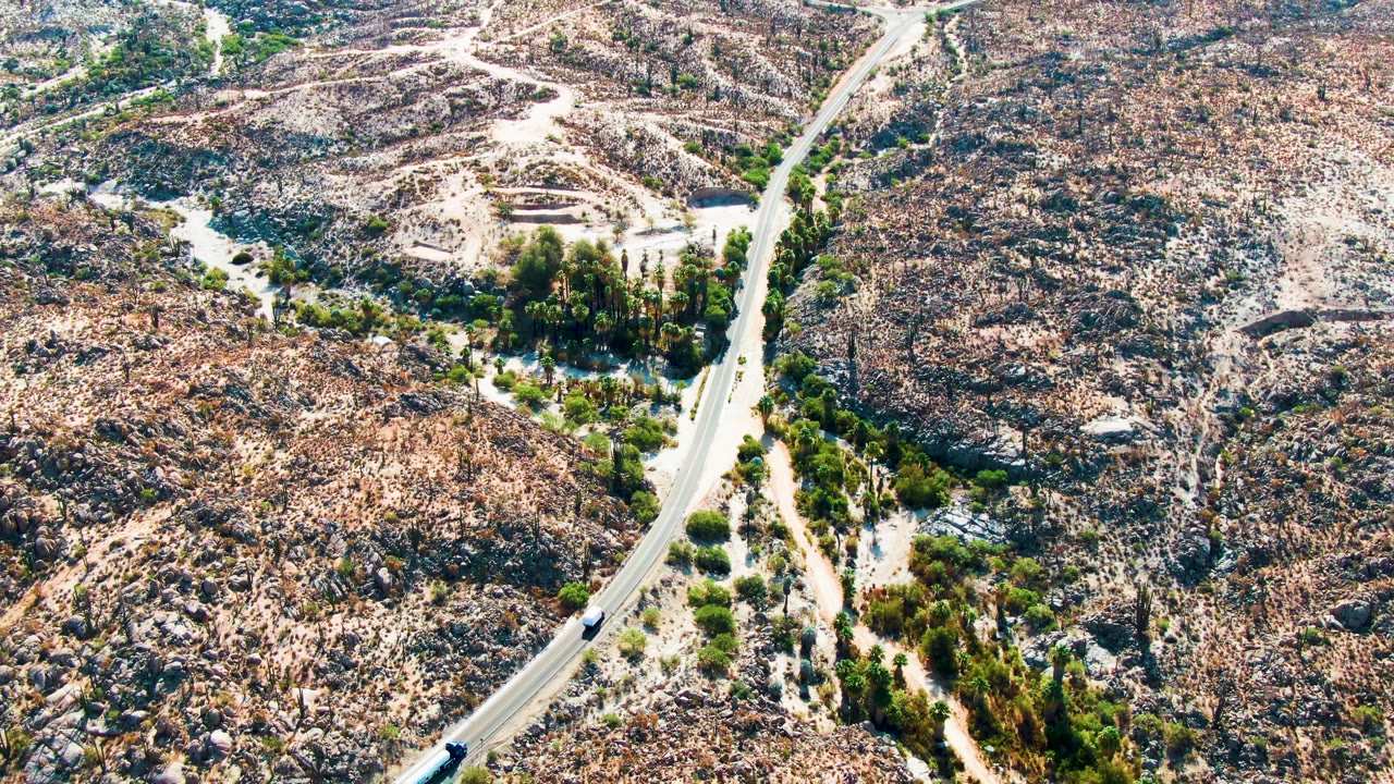 Aerial view of a winding desert road with a vehicle near the lower left.