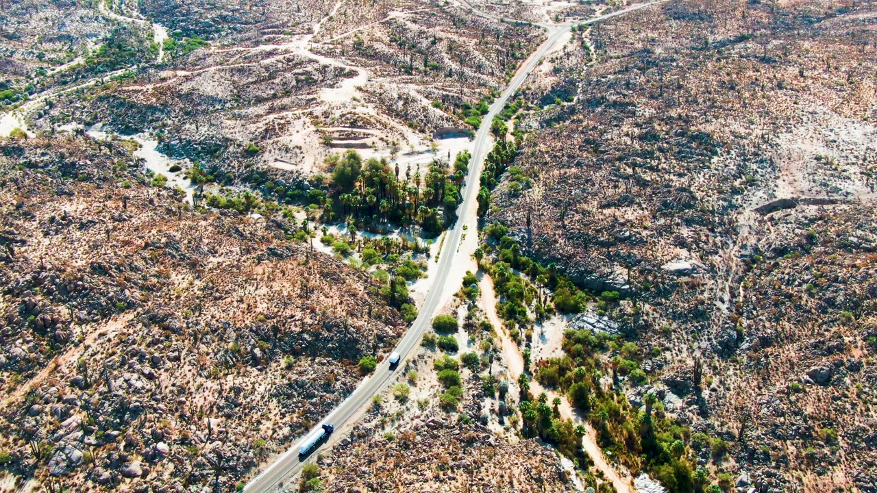 Aerial view in Catavina BC, Mexico with the vehicle progressing along the lower-left road curve, pale dirt tracks crossing the rocky desert, and no visible people.