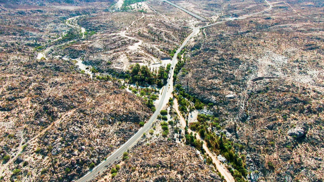 High aerial view in Catavina BC Mexico with the road running from the lower left into dry rocky ground, dirt tracks, scattered vegetation, and no visible people.