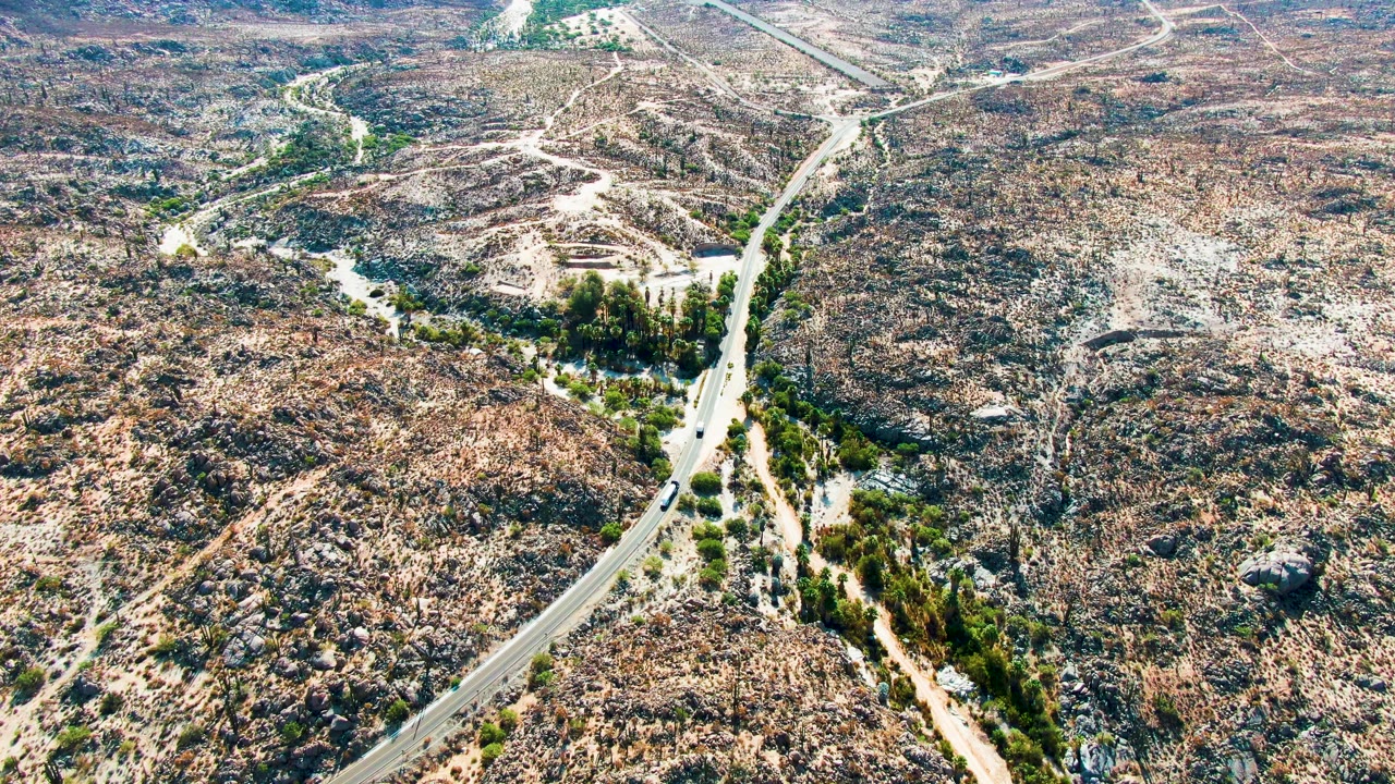 Aerial view over Catavina BC Mexico showing a winding road crossing rocky brown desert with scattered green vegetation and no visible people.