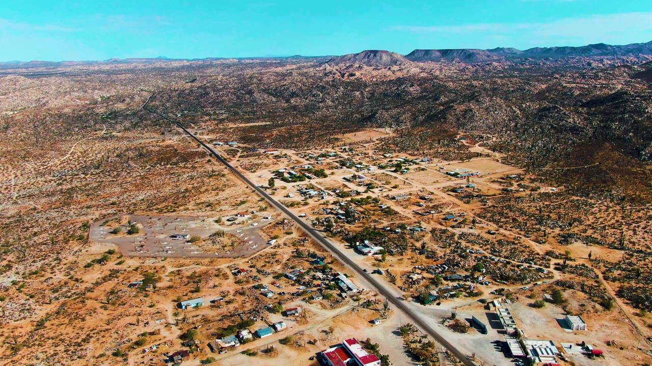 Aerial desert landscape with a small settlement, paved road, and mountains.