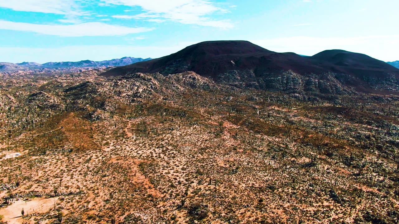 Wide aerial desert landscape with a dark mountain and bright sky