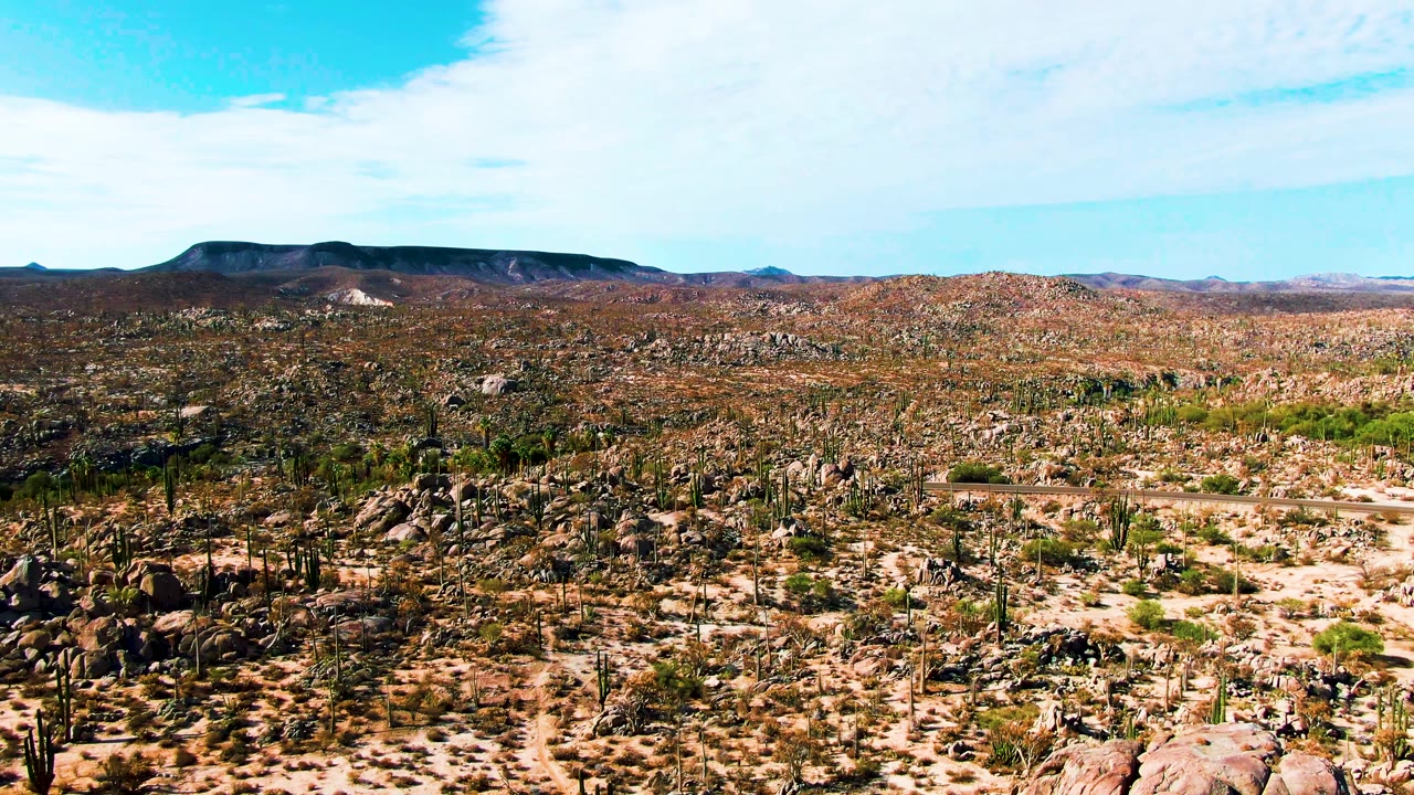 Opening view of Catavina BC Mexico showing a cactus-dotted rocky desert plain under bright blue sky with thin clouds and no visible people.