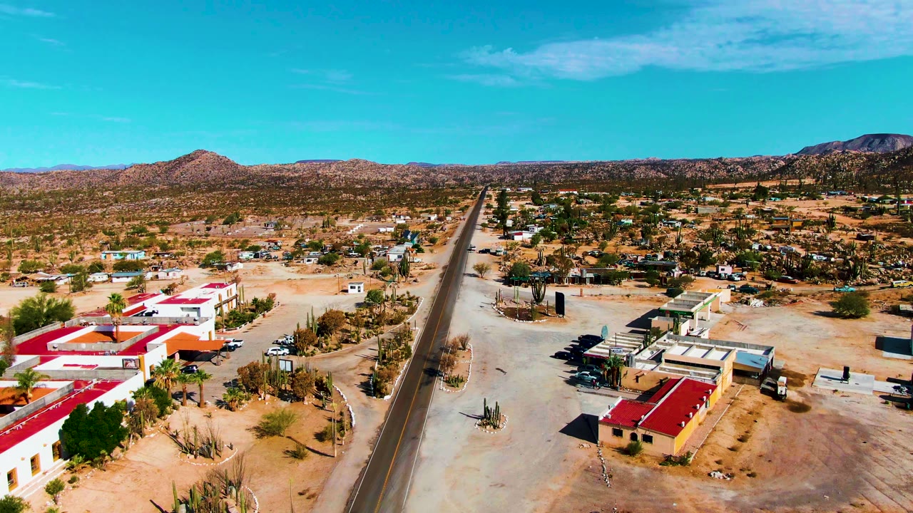 Aerial view of desert buildings, cacti, and a paved road under blue sky.