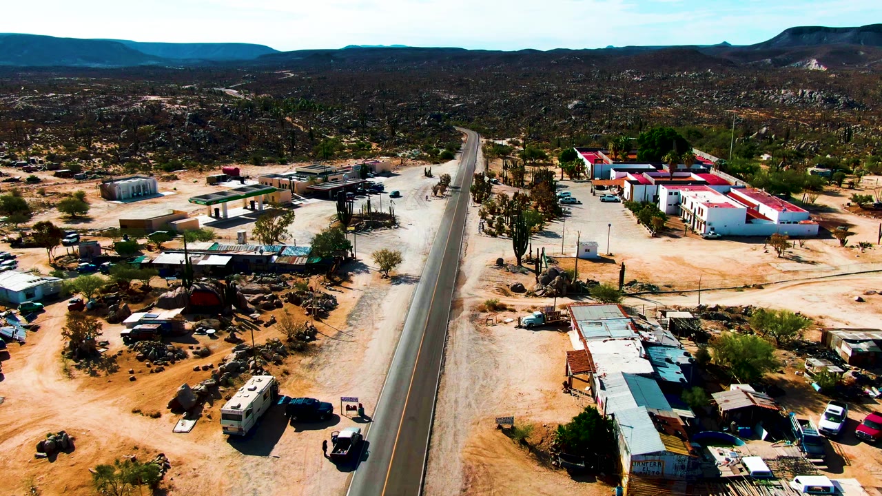 Roadside desert lots with sheds, parked vehicles, cacti, and hills beyond.