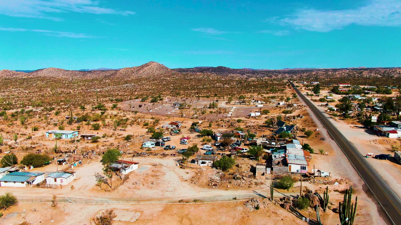 Aerial desert settlement with paved road and cactus foreground