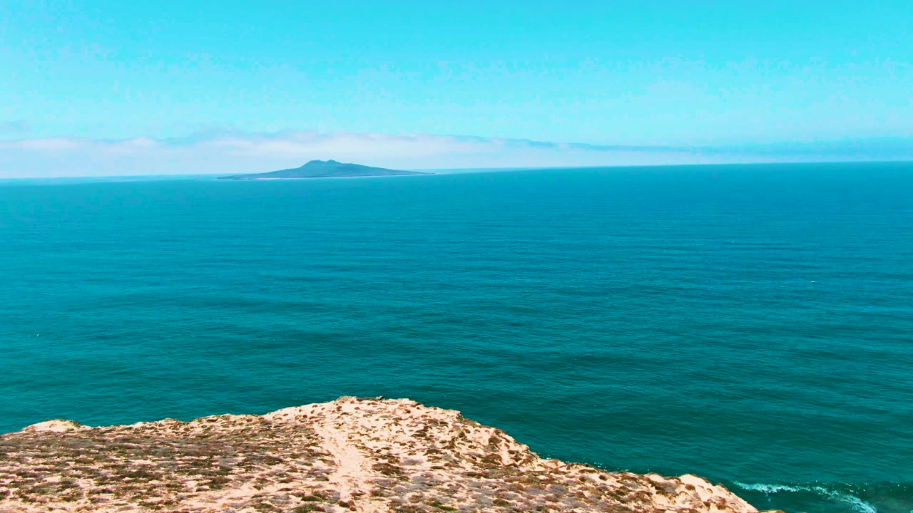 Turquoise ocean beyond a rocky cliff with a distant island on the horizon.