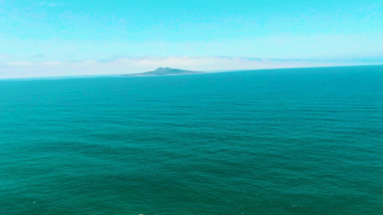 Wide turquoise ocean in San Quintin BC Mexico with a small distant island left of center on the horizon and no visible people.