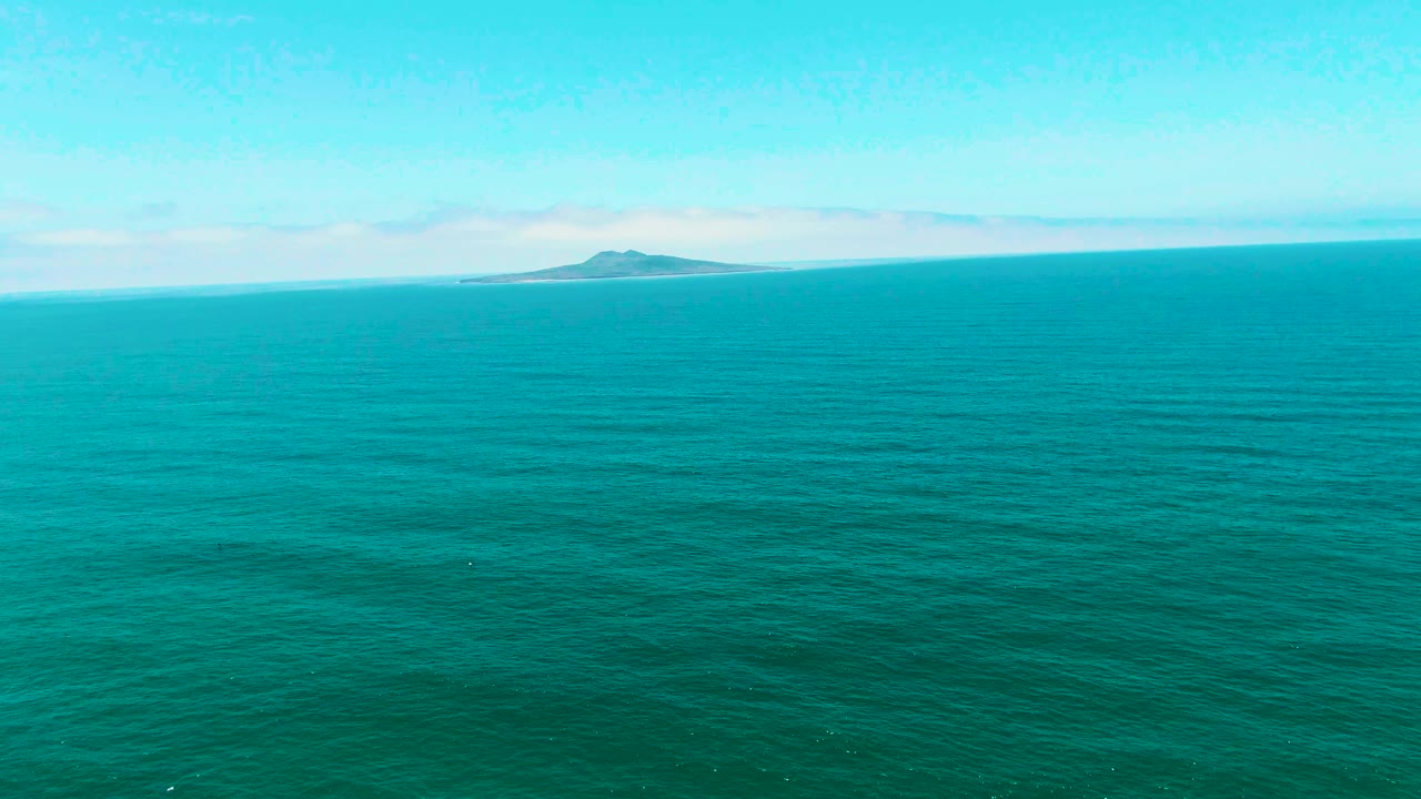 Calm turquoise sea in San Quintin BC Mexico with low ripples across the foreground and a small island near the center horizon, with no visible people.