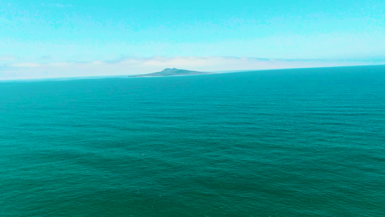 Open turquoise water in San Quintin BC Mexico under a bright sky, with the distant island slightly right of center and no visible people.