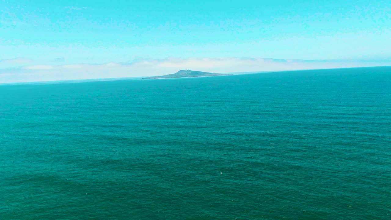 Opening frame of turquoise ocean near San Quintin BC, Mexico, with a small island low on the horizon, light clouds above, and no visible people.