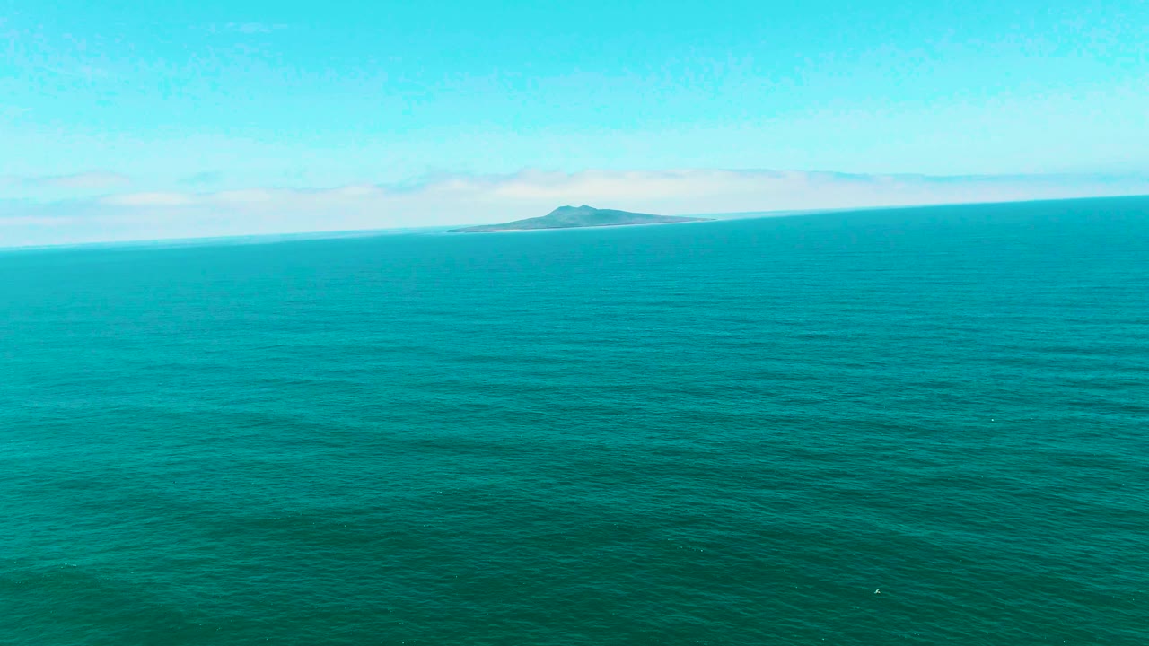 Calm turquoise water stretches toward a distant island beneath scattered clouds.