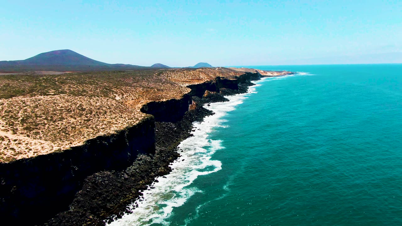 Dry cliff coast with waves foaming against dark rocks.