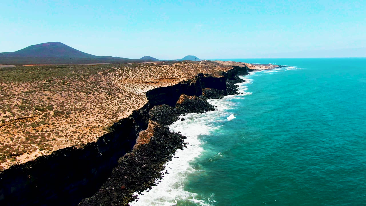 Aerial view of rocky coastal cliffs beside turquoise ocean.