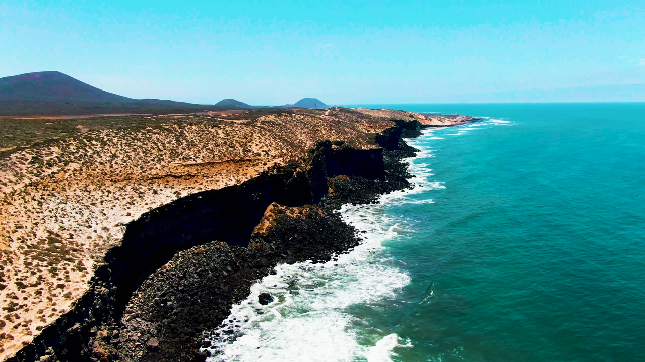 Aerial view of arid cliffs beside turquoise ocean water