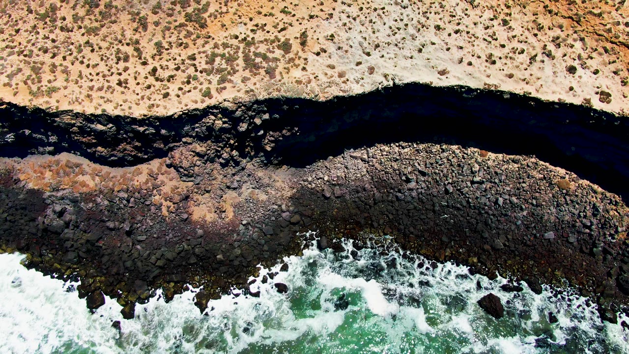 At 0:03, San Quintin BC Mexico appears from above with a broader pale sand strip, dark river water, mottled rocks, active white surf, and no visible people.