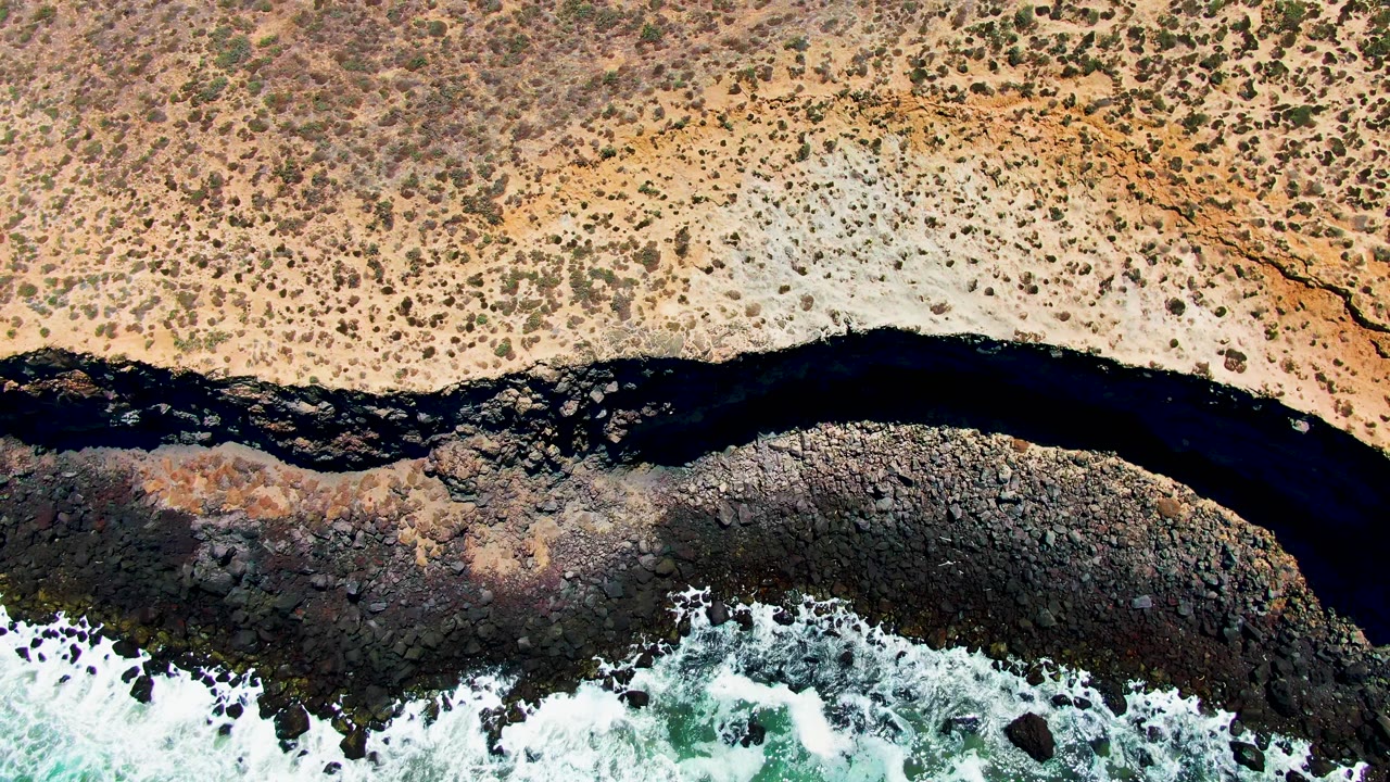 Dry coastal scrub above dark river and foaming rocky shore