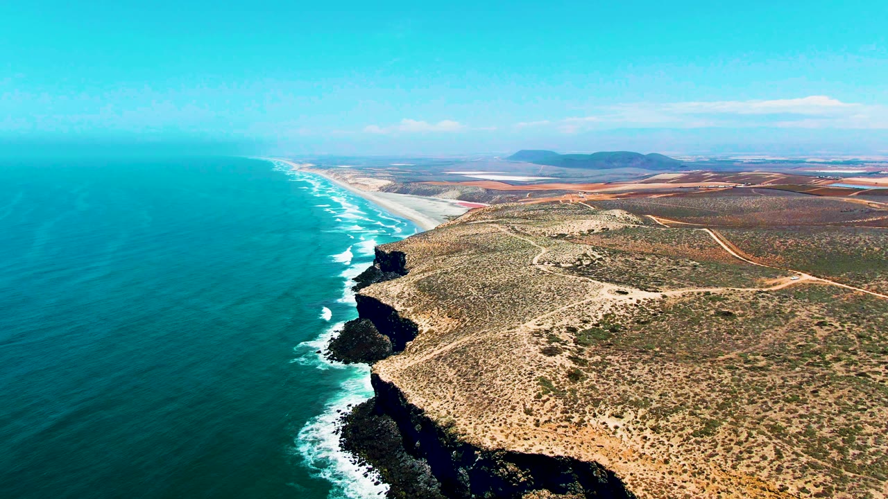 Aerial view of turquoise ocean beside rocky coastal cliffs and dry scrubland.