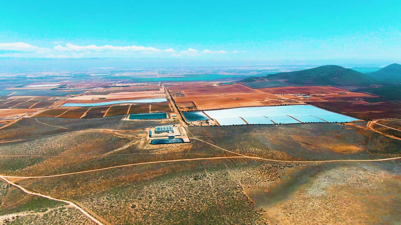 Aerial reservoir complex surrounded by dry land, dirt roads, and distant hills.