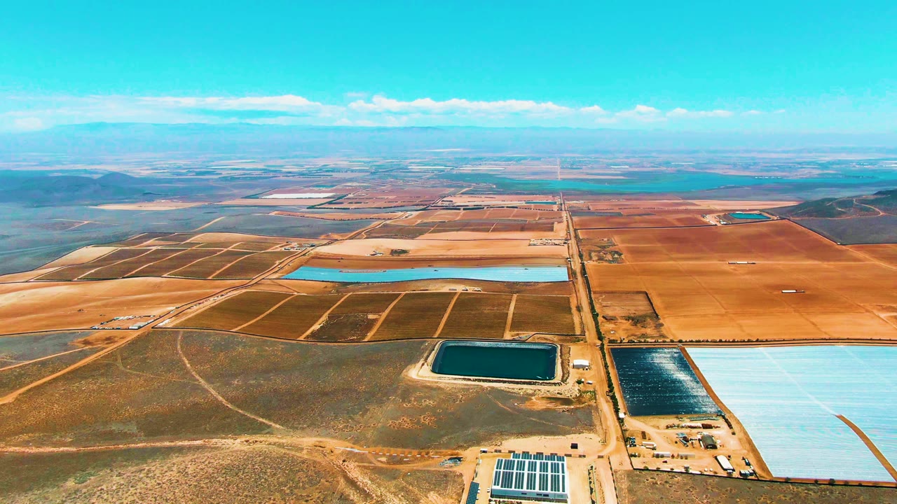 Aerial landscape of agricultural plots, reservoirs, solar panels, and distant hills.