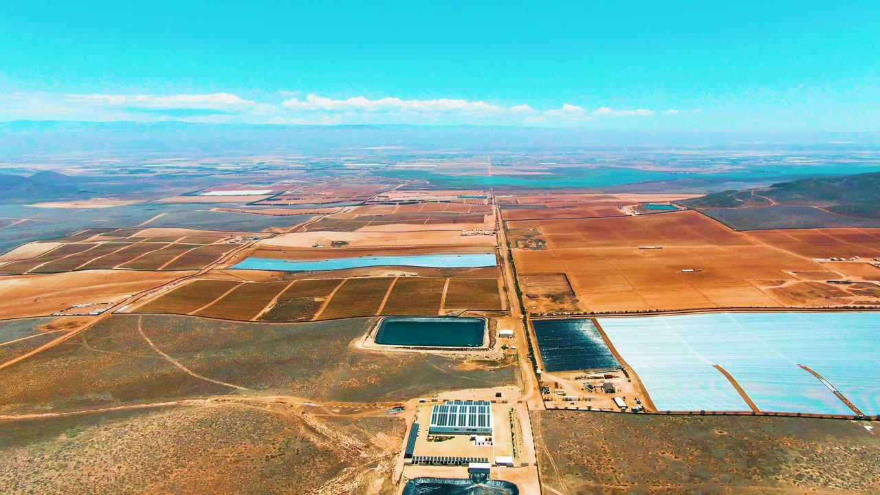 Aerial landscape with water reservoirs, a solar facility, fields, and road lines.