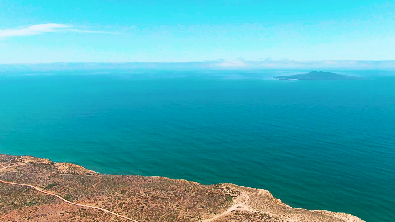 At three seconds, the San Quintin BC Mexico view holds on open ocean with faint surface texture, a distant island along the horizon, scrubby cliff land at the lower edge, and no visible people.