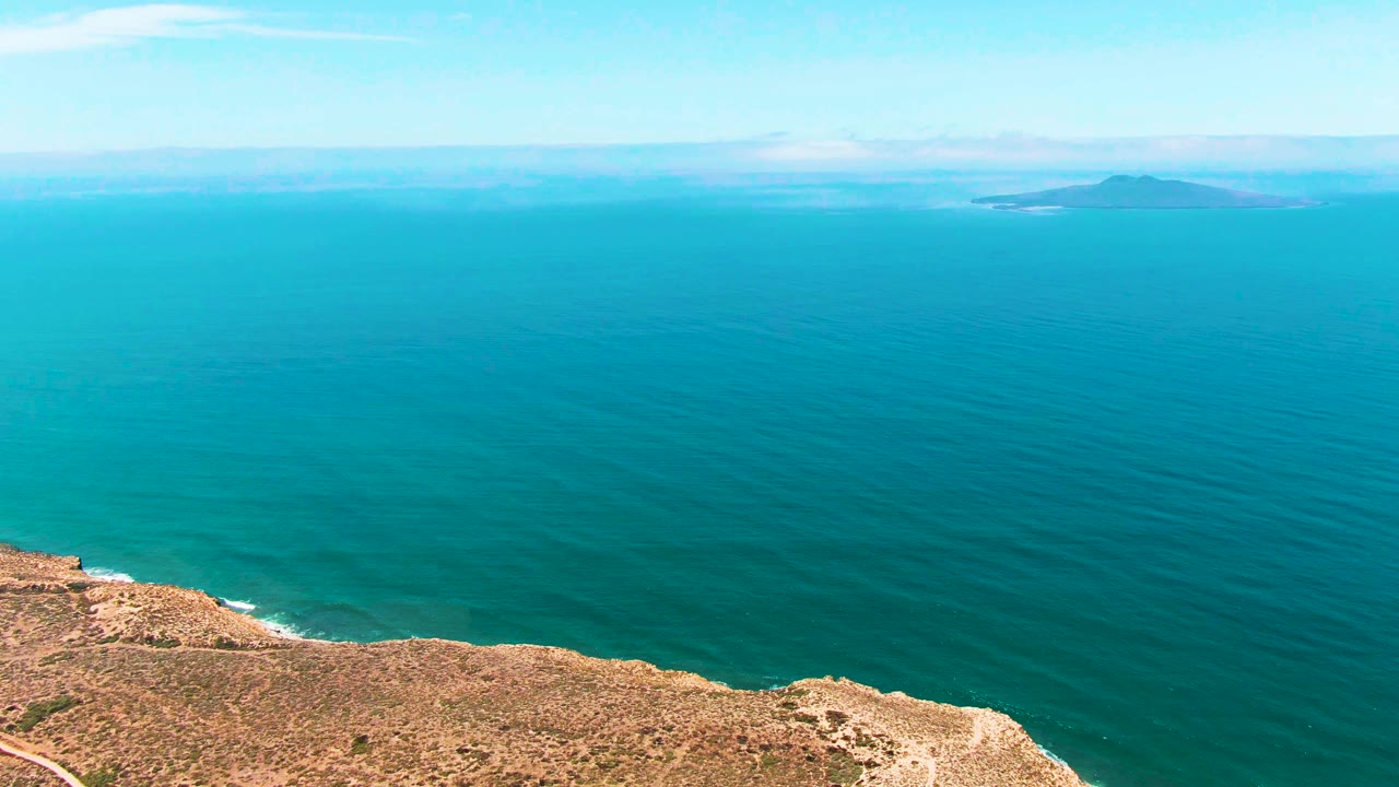 Dry cliff edge below a broad turquoise sea and distant islands