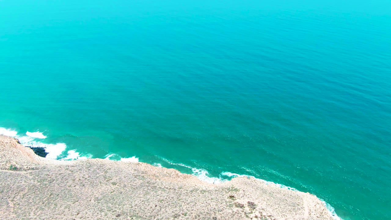 Open turquoise water above a narrow strip of rocky coast and surf.