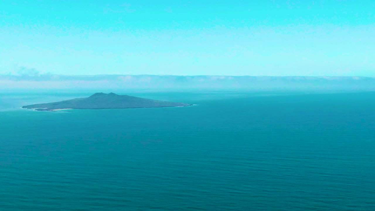 Small dark island at left-center beyond calm turquoise water.