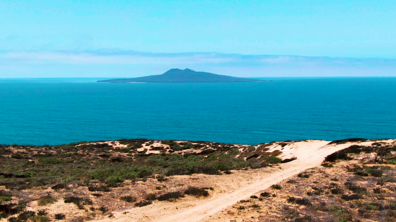Sandy dune path leading toward blue ocean and distant island