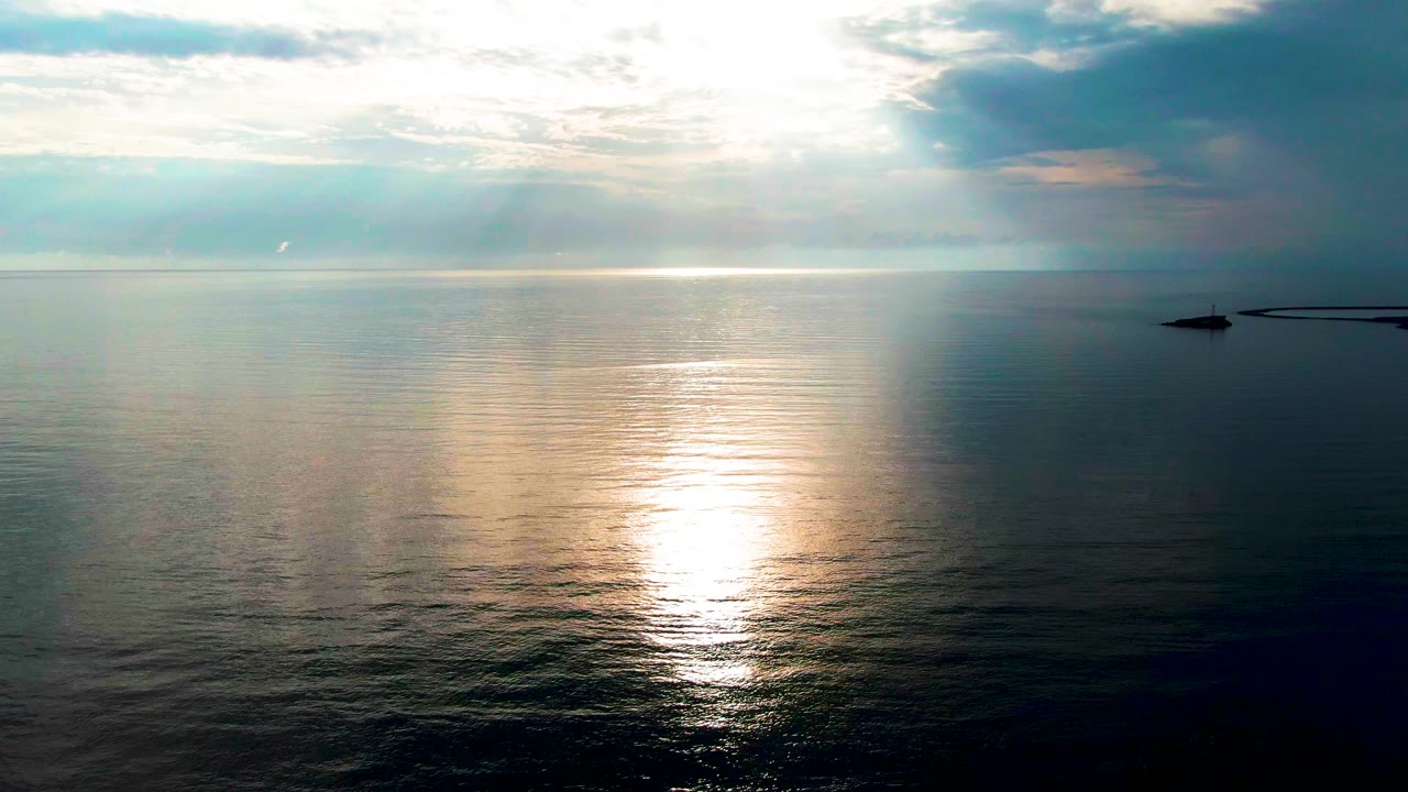 At one second, the Santa Rosalia ocean view holds a bright vertical reflection on gentle ripples, with pale clouds above and a darker cloud mass on the right, no visible people.
