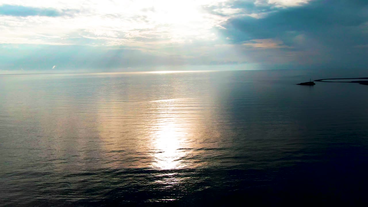 Sunlight reflected on calm ocean under clouds with a small structure at right.
